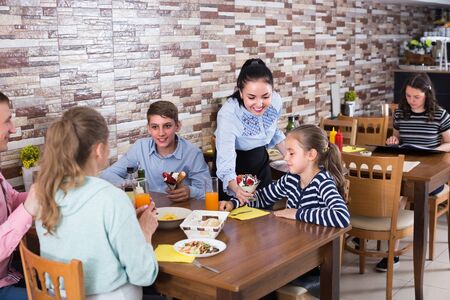 Adult female is bringing delicious dessert to young visitors of family cafe.の写真素材