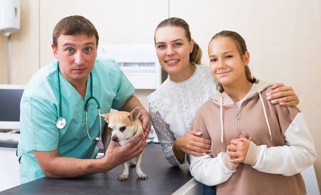 Cheerful mother and daughter visiting veterinarian clinic with their puppyの写真素材