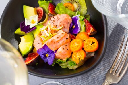 Delicious ceviche of salmon with kiwi fruit, avocado, kumquat and figs garnished with heartsease flowers の写真素材