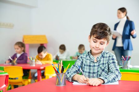 Portrait of little diligent schoolboy writing at lesson in elementary schoolの写真素材