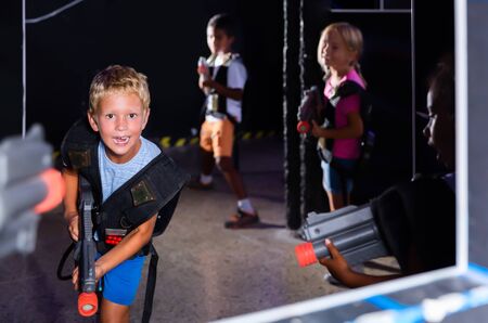 Emotional teen boy with laser pistol playing laser tag with friends on dark labyrinthの写真素材