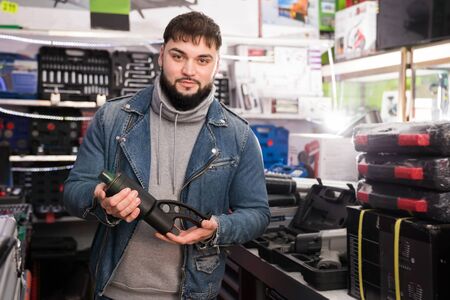 Young man hardware shop visitor selects electric toolの写真素材
