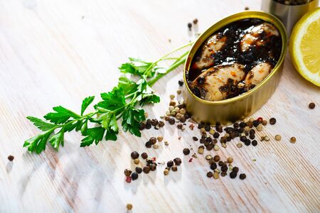 Closeup view of opened can of chipirones in ink on wooden table with fresh parsley, lemon and spicesの写真素材