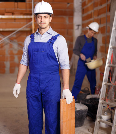 Two builders in work wear doing repair in brick private house