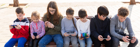 Group of children playing with smartphones outdoors at sunny spring day