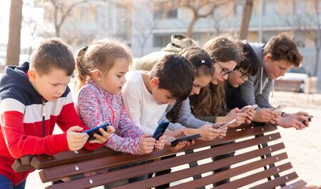 Group of boys and girls addicted in their phones spending time together outdoorsの写真素材