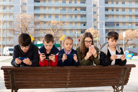 Group of children playing with smartphones outdoors at sunny spring day