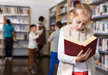 Portrait of intelligent preteen girl browsing textbooks in school libraryの写真素材