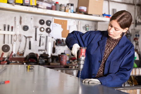 Young woman  worker working   with metal sheet and using  electric drill  in workshop