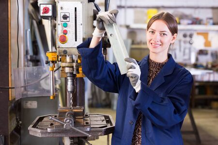 Confident young workwoman drilling metal parts on stationary bench drill in metalworking workshopの写真素材