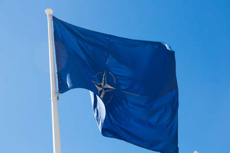 Flag of NATO on flagstaff waving against blue skyのeditorial素材