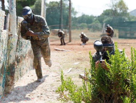Paintball player in camouflage and mask aiming with gun in shootout outdoorsの写真素材