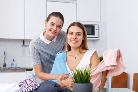 Portrait of two girls showing each other and trying clothes in kitchen interiorの写真素材