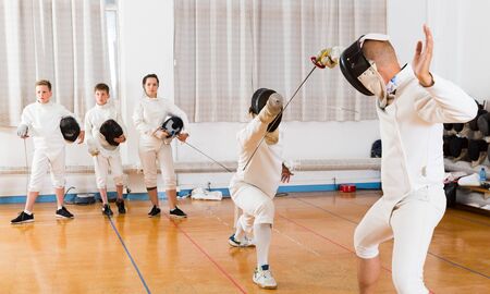 Young fencers watching at fencing duel with foils of two professional coaches in gymの写真素材
