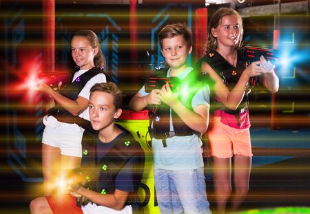 Cheerful teen girls and boys with laser pistols posing together in dark laser tag labyrinthの写真素材