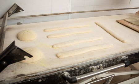 Proofing loaves of bread and baguettes on working surface in baker workshop. Traditional baking techniqueの写真素材