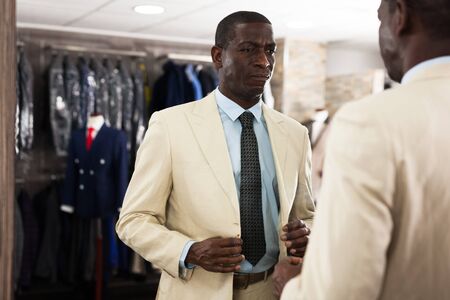 Confident male customer choosing fashion beige suit in mens storeの写真素材