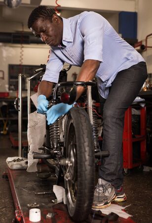 Afro american worker fixing failed motorcycle in workshopの写真素材