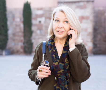 Smiling mature female is walking and talking by phone