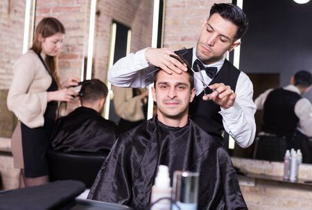 Professional hairdresser man doing styling of handsome guy at barber shopの写真素材