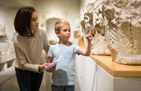 Attentive young woman with school age boy visiting sculptures exposition in museum, pointing to somethingのeditorial素材