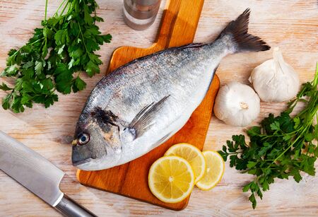 Whole fresh gilthead bream on wooden surface with vegetables, lemon and spices ready for cookingの写真素材