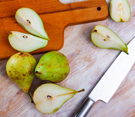 Ripe pears and knife on wooden cutting board