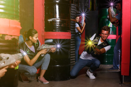Portrait of happy young friends playing laser tag  game  with laser guns in dark room