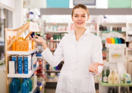 Portrait of smiling pleasant positive female druggist in white coat working in pharmacyの写真素材