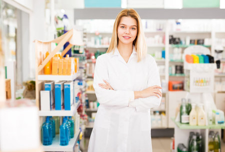 Cheerful woman pharmacist standing with arms crossed in interior of pharmacyの写真素材
