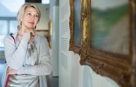 Glad cheerful  smiling female visitor looking at artwork painting in the museum indoorsの写真素材