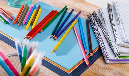 Closeup of colored lead pencils and wax chalks for drawing with paper and sketchpads on wooden surfaceの写真素材