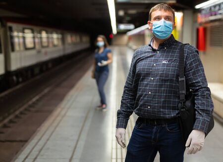 Casual man wearing medical mask and rubber gloves waiting for train in platform of underground station. New life reality during COVID 19 pandemicの写真素材