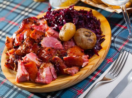 Sliced baked pork shank served with vegetable garnish of braised red cabbage on wooden board

の写真素材