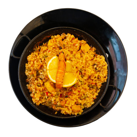 Delicious seafood paella - savory rice dish with shrimps and clams served with lemon slice in traditional paella pan. Isolated over white backgroundの写真素材