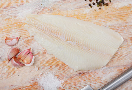Fresh halibut fillet on wooden surface with seasonings prepared for cooking