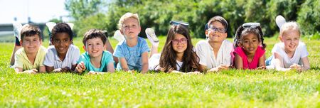 Happy team of friends children resting on grass together in parkの写真素材