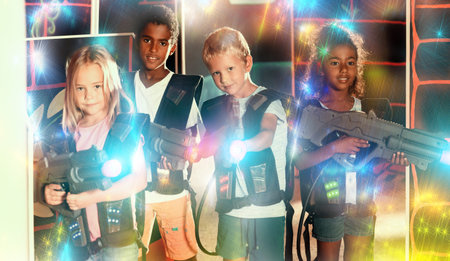Modern teenage girl and boys with laser guns playing laser tag on dark arenaの写真素材
