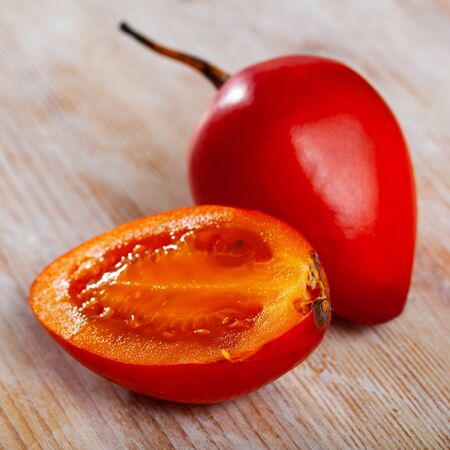 Whole and halved fresh tamarillo fruits on wooden backgroundの写真素材