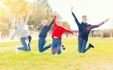 Four joyful teens jump on a spring lawnの写真素材