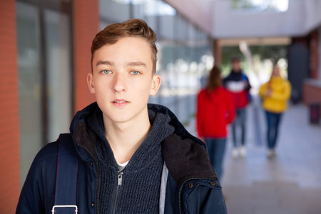 Portrait of teen boy with backpack walking to college campus on spring day