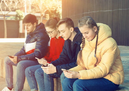 Four teenagers chatting on their smartphone on walking