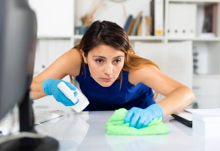 Young  mexican woman wearing uniform cleaning table with spray at company officeの写真素材