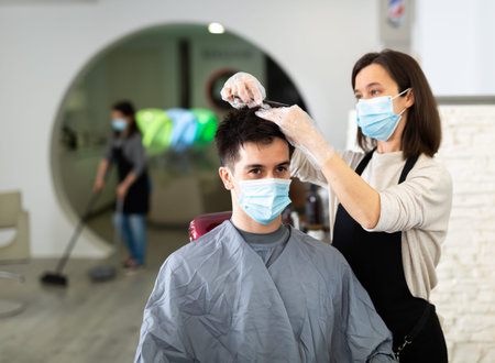 Man client in mask during hair cut by professional hairdresser in mask at beauty salon