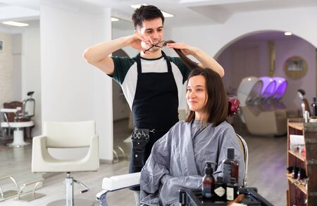 Portrait of male hairdresser and female client getting haircut at local hair studioの写真素材