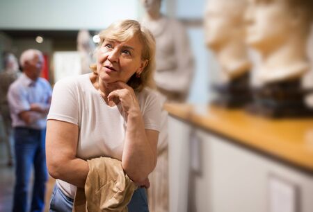 Senior woman looking at exhibit on exposition of historical museumの写真素材