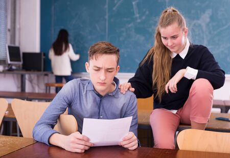 Thoughtful university students sitting at desk and preparing for exams together in classroomの写真素材