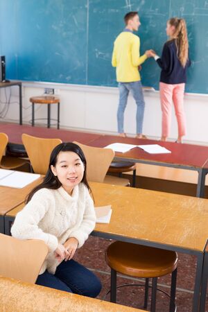 Portrait of female chinese student in auditorium, students writing on whiteboardの写真素材