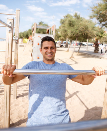 Athletic male doing workout on fitness station exercising in morning outdoors