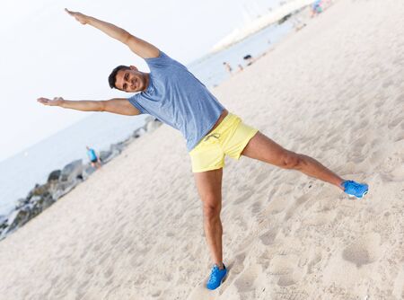 Young sporty man doing doing exercises on ocean beach at daytimeの写真素材